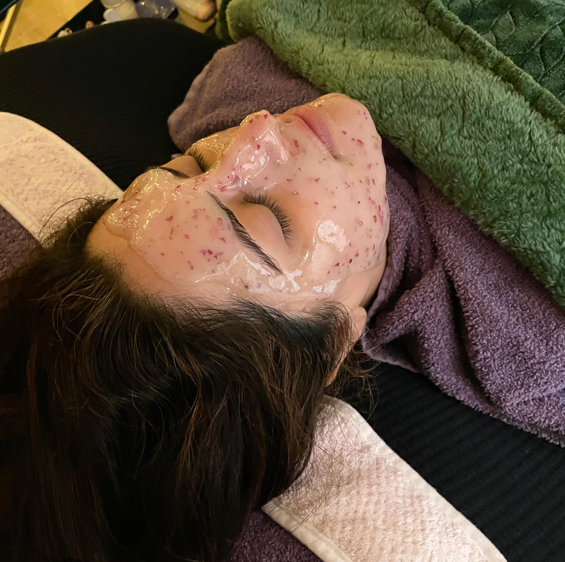 a woman getting a facial, relaxing on a recliner with a hydrojelly mask